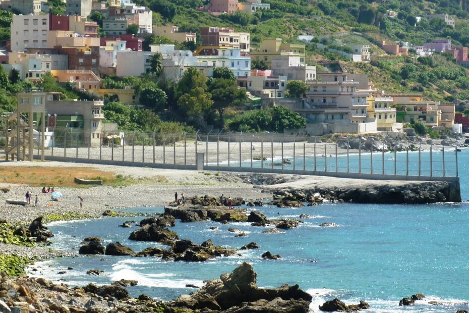 Valla fronteriza junto al mar entre Ceuta y Marruecos, con el pueblo de Beliones al fondo