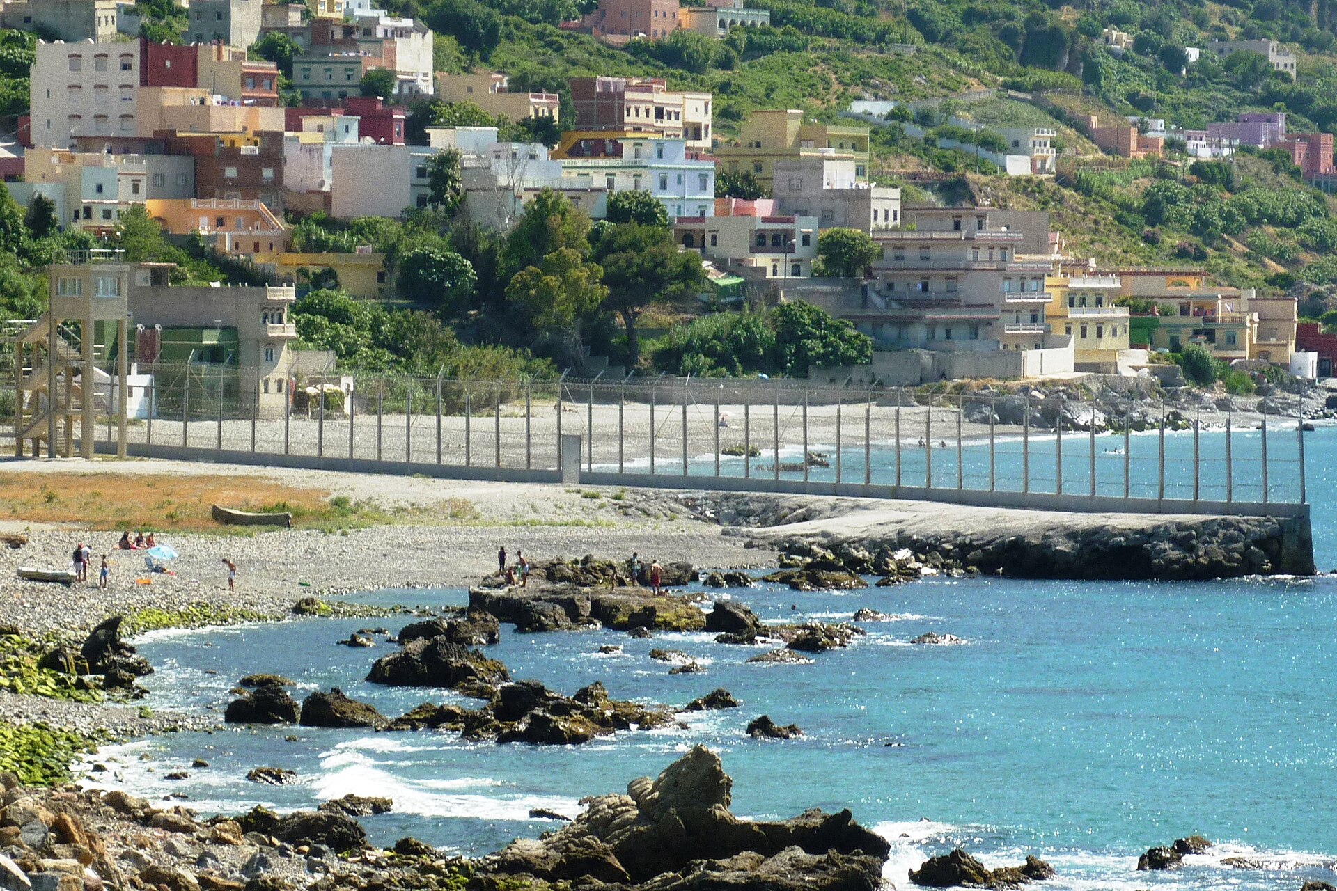 Valla fronteriza junto al mar entre Ceuta y Marruecos, con el pueblo de Beliones al fondo